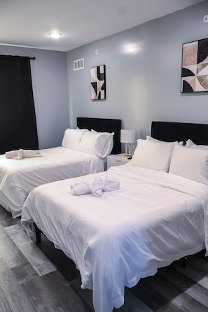 Habitación de hotel con dos camas, una mesita de noche, una lámpara y arte abstracto en la pared.