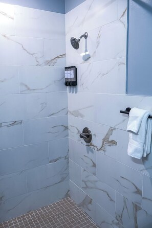 Un baño con azulejos de mármol, ducha, toallero y panel de control.