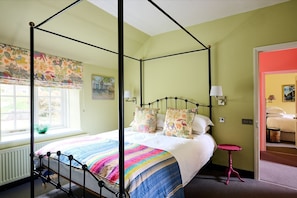 Una cama con dosel y un edredón a rayas de colores, una ventana con vistas a la vegetación y un cuadro en la pared.