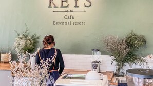 A cafe named KEYS with a sign on the wall, a woman standing in front of it, and various plants and kitchen appliances on the counter. - Keys Essential Resort (Pai)