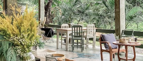 Un área de estar al aire libre con mesa y sillas, rodeada de vegetación.