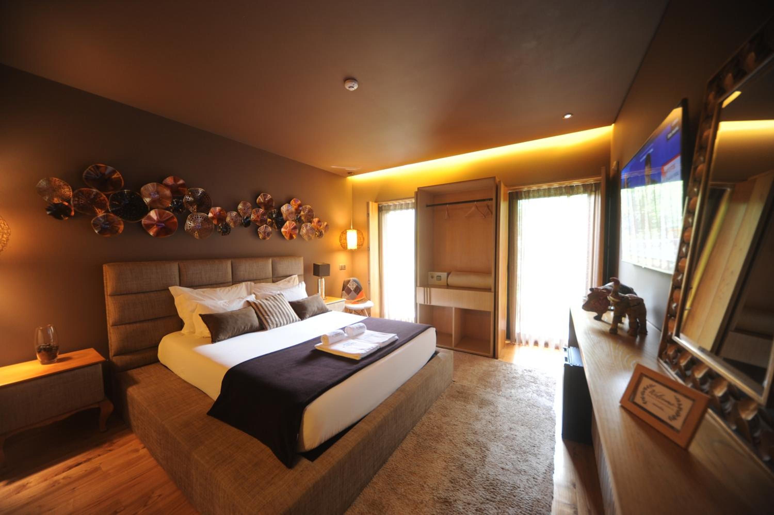 Habitación de hotel con una cama grande, una mesita de noche, una lámpara de pared, un armario y un espejo.