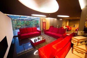 A modern living room with red sofas, a glass coffee table, and a view of greenery outside. - Rio Moment S (Castelo de Paiva)