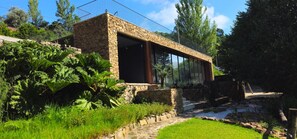 A stone building with large windows, surrounded by lush greenery and a stone pathway. - Rio Moment S (Castelo de Paiva)