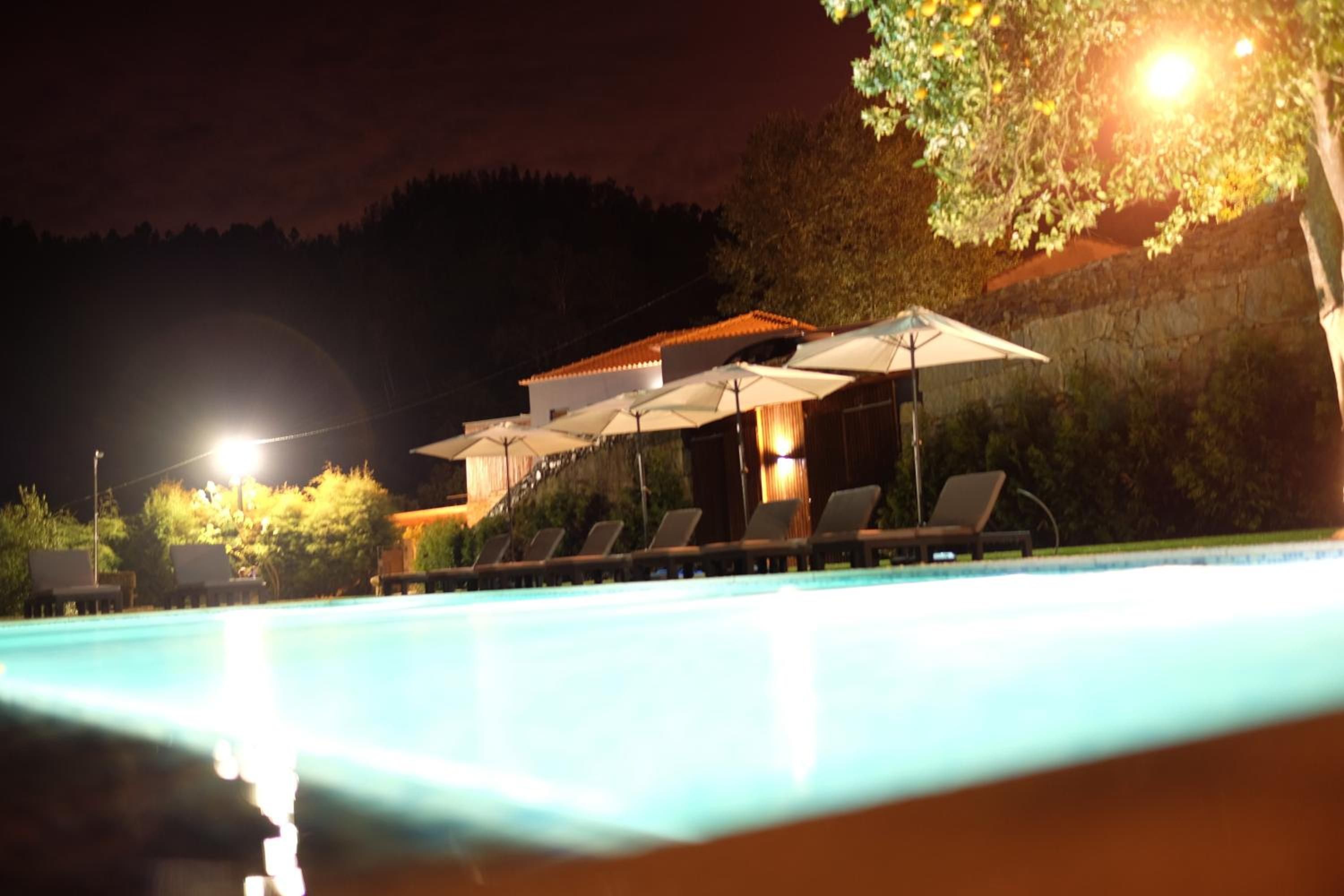 A swimming pool with lounge chairs and umbrellas, surrounded by trees and a building.