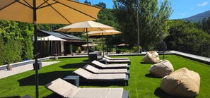 A poolside area with lounge chairs and umbrellas, surrounded by greenery and a building. - Rio Moment S (Castelo de Paiva)