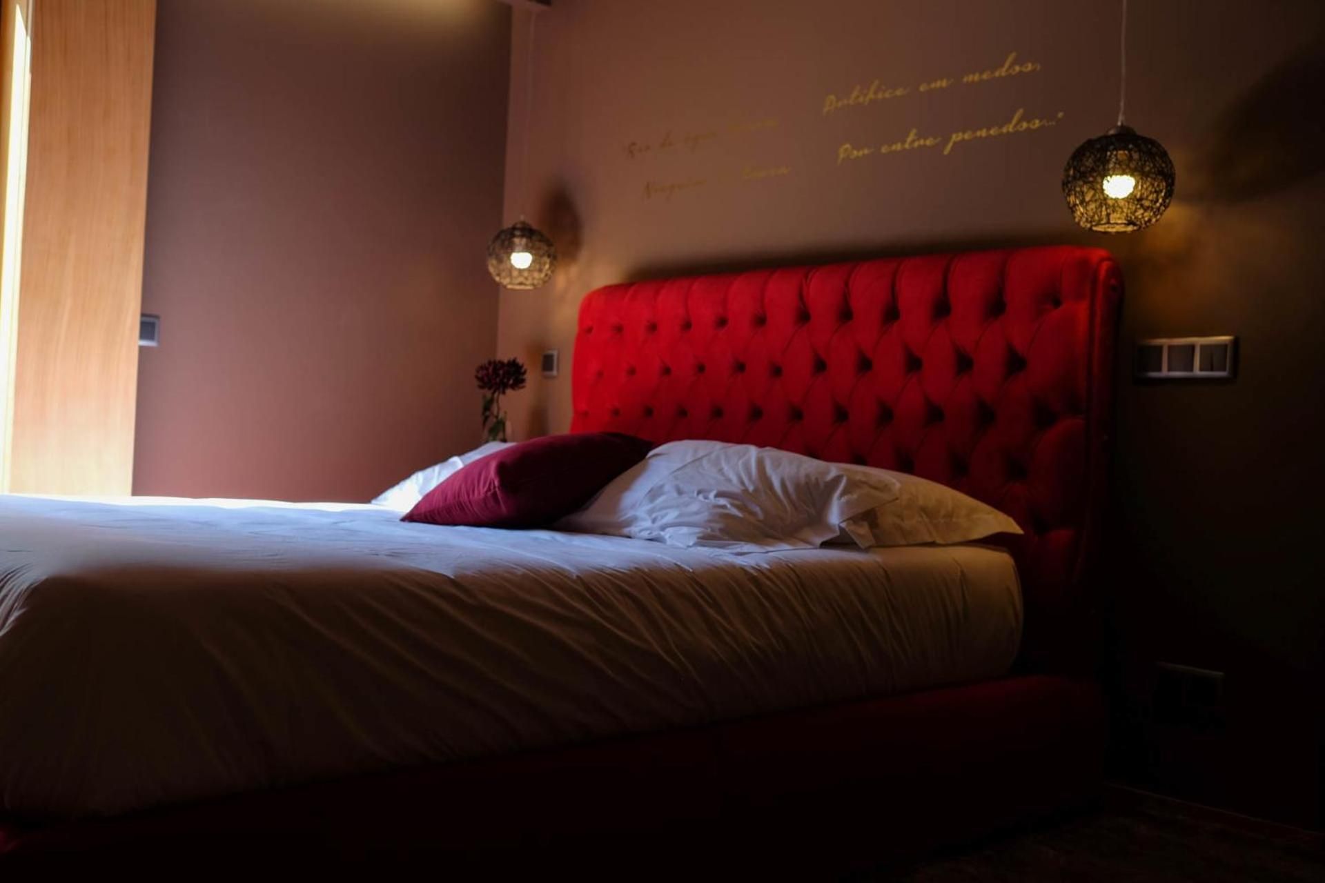 A bedroom with a red tufted headboard, a bed with white and red bedding, and two pendant lights.