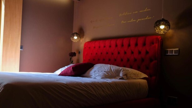 Una camera da letto con testiera imbottita rossa, un letto con biancheria rossa e bianca e due lampade a sospensione.