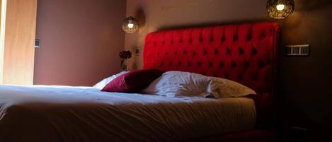 A bedroom with a red tufted headboard, a bed with white and red bedding, and two pendant lights.