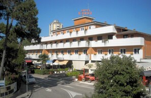 A multi-story hotel with balconies, a sign indicating 'HOTEL S. CRUZ,' and outdoor seating areas. - Hotel Santa Cruz (Lignano Sabbiadoro)