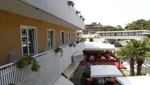 Un hotel con posti a sedere all'aperto, facciata in legno e tenda da sole bianca.