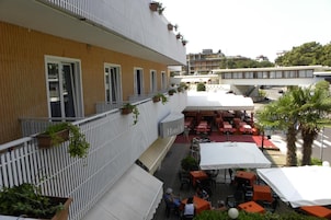 Hotel con terraza exterior, fachada de madera y toldo blanco.