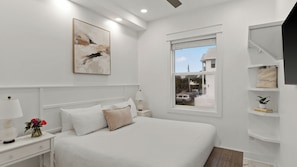 Ein Schlafzimmer mit Bett, Nachttischen, einer Lampe, einem Gemälde, einem Fenster und Blick ins Freie.