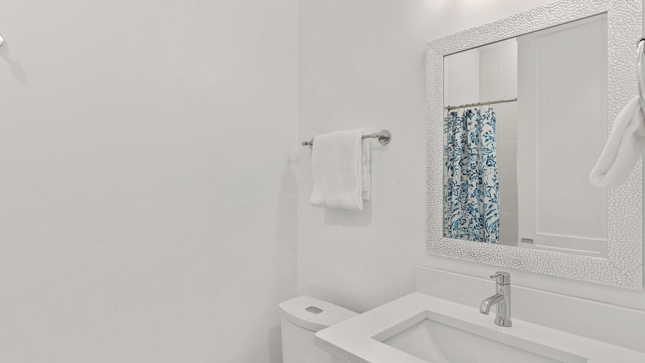 A bathroom with a white sink, a mirror with a textured frame, and a shower curtain with a floral pattern.
