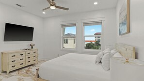 Quarto com cama, penteadeira, televisão e janelas com vista.