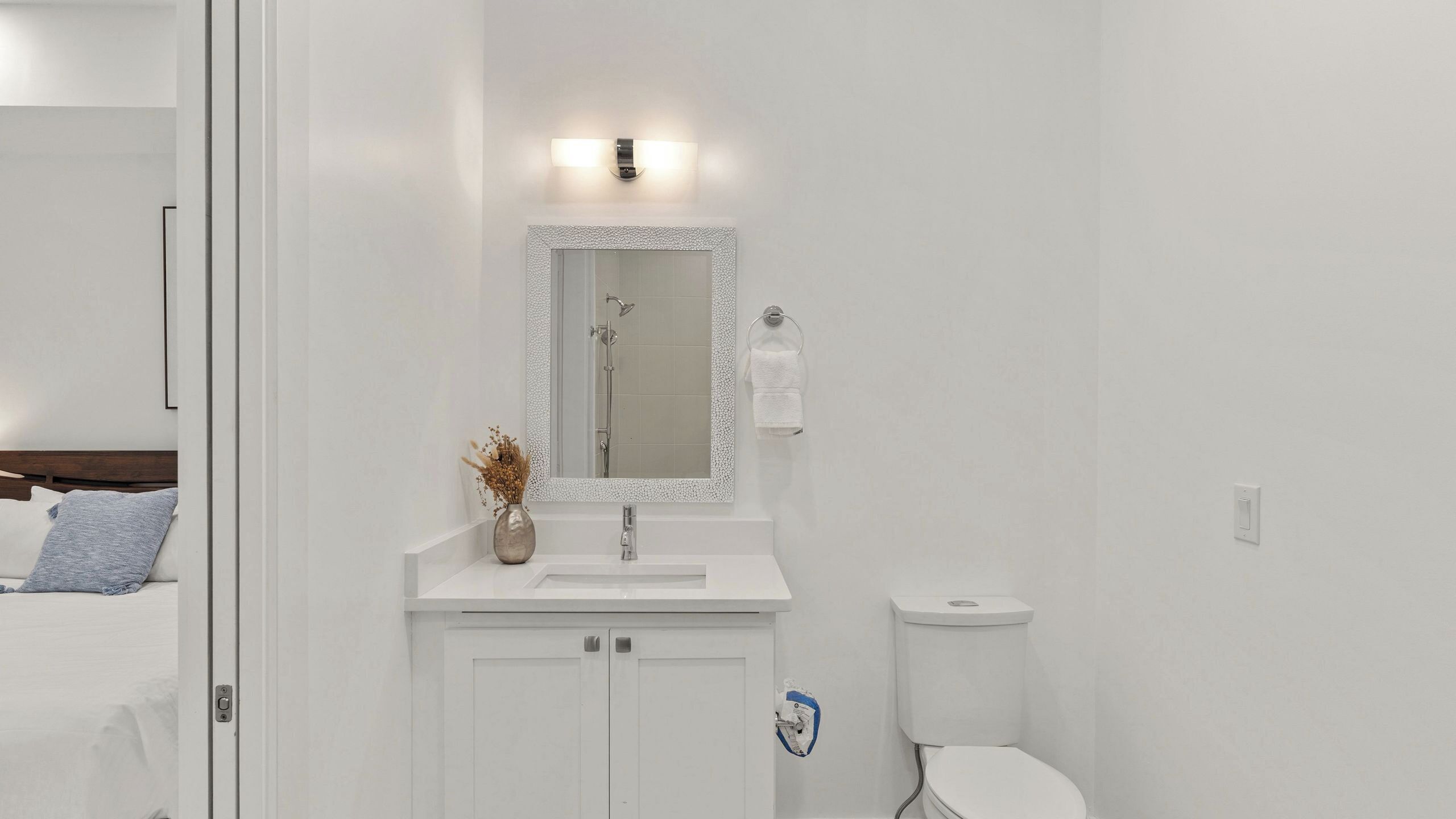 Une salle de bain avec un lavabo blanc, un miroir doté d’un cadre texturé, un porte-serviettes et des toilettes.