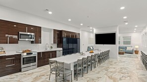 Uma cozinha moderna com uma ilha central, eletrodomésticos embutidos e uma área de jantar com uma mesa comprida e cadeiras.