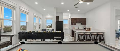Une cuisine moderne avec des meubles en bois foncé, un îlot central doté de tabourets et une table de billard, avec une table de baby-foot en premier plan.