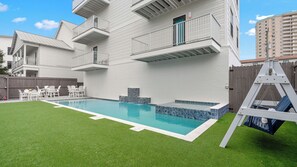A modern two-story building with a swimming pool, outdoor seating, and a swing set. - Emerald Retreat by Avantstay Sleeps 44 + Pool + Spa Theater + Game Room Walk to Beach (Miramar Beach)