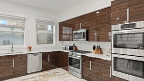 A modern kitchen with stainless steel appliances, wooden cabinetry, and a large window. - Emerald Retreat by Avantstay Sleeps 44 + Pool + Spa Theater + Game Room Walk to Beach (Miramar Beach)