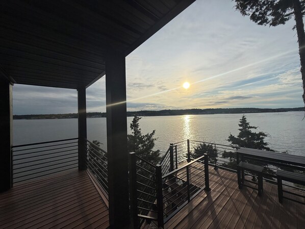 Une terrasse en bois avec une rambarde donnant sur une étendue d’eau au coucher du soleil.