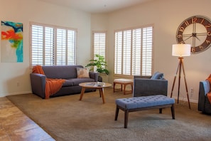 Ein Wohnzimmer mit Sofa, Sessel, Hocker, Couchtisch und Lampe.