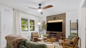 Un salon comprenant un canapé, des fauteuils, une table basse, un téléviseur, une cheminée et un ventilateur de plafond.