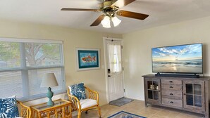 A living room with a ceiling fan, a television, wicker furniture, a framed fish painting, and a view of the ocean on the TV. - 2BR Coastal Cottage – Minutes to Beach & Bay (Englewood)