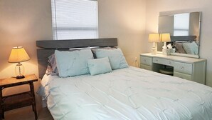A bedroom with a bed, bedside table, lamp, dresser, mirror, and window with blinds. - 2BR Coastal Cottage – Minutes to Beach & Bay (Englewood)