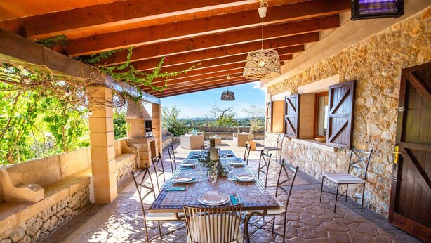 Un patio al aire libre con suelo de piedra, una mesa lista para comer y una pared de piedra con ventanas.