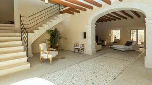 Ein großzügiger Wohnbereich mit Steinfliesen, einer Treppe mit Holzwandlaufgeländer und einer Sitzecke mit Sofa und Sesseln.