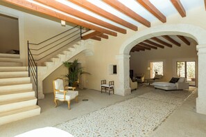 A spacious living area with a stone-tiled floor, a staircase with a wooden railing, and a seating area with a sofa and chairs. - Casa Buger - Three Bedroom Villa, Sleeps 6 (Mallorca)