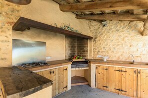 A rustic kitchen with a stone wall, wooden cabinets, a stainless steel range hood, and a built-in grill. - Casa Buger - Three Bedroom Villa, Sleeps 6 (Mallorca)