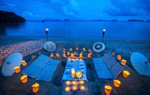 Un montaje para comer frente al mar, con una mesa, sillas y velas.