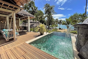 Eine Holzterrasse mit Pool, einer Reetdachkonstruktion und Blick auf den Strand.