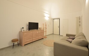 Ein modernes Wohnzimmer mit Flachbildfernseher, Holzschrank, rundem Teppich und einem beigefarbenen Sofa.