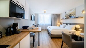 A modern hotel room with a bed, desk, and seating area, equipped with a coffee maker and a flat-screen TV. - Bodenseezeit Apartmenthotel Garni (Wangen im Allgäu)