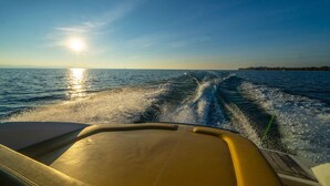 A boat's wake on a body of water with a clear sky and sun. - Bodenseezeit Apartmenthotel Garni (Wangen im Allgäu)
