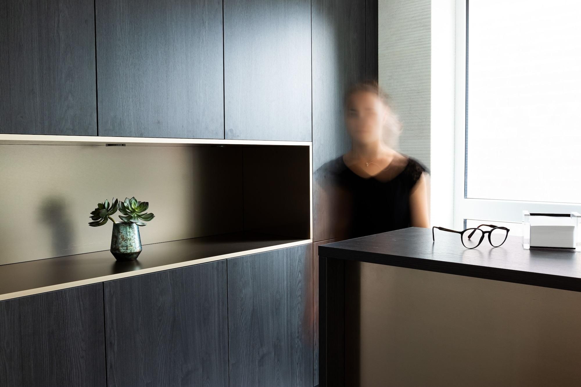 Ein modernes Interieur mit dunklen Holzsäcken, einer kleinen Pflanze auf einem Regal und einem Brillenpaar auf einem Tisch.