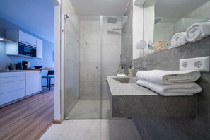 Um banheiro moderno com chuveiro, uma toucador com espelho e um porta-toalhas.