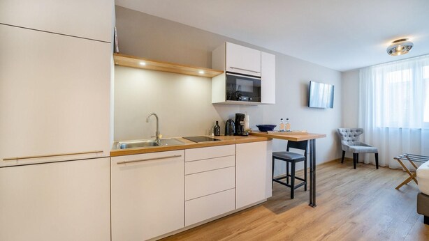 A modern kitchen with a built-in oven, a microwave, and a sink. There is a wooden countertop, a chair, and a table. - Bodenseezeit Apartmenthotel Garni (Wangen im Allgäu)