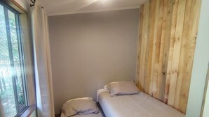 Una habitación pequeña con dos camas, una ventana y paneles de madera en una pared.