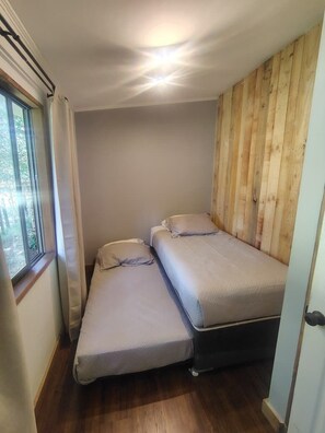 Petita habitació amb dos llits, una finestra i panells de fusta a una paret.