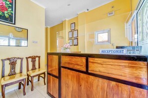 A reception area with a wooden reception desk, two wooden chairs, a clock, framed certificates, and a window. - Flagship 90768 Endrayanti Inn Syariah (Yogyakarta)