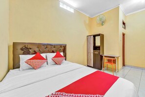 A hotel room with a bed, a desk, a chair, a mirror, and a fan. - Flagship 90768 Endrayanti Inn Syariah (Yogyakarta)