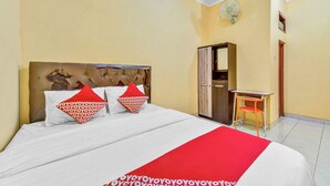 A hotel room with a bed, a desk, a chair, a mirror, and a fan. - Flagship 90768 Endrayanti Inn Syariah (Yogyakarta)