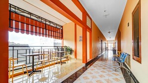 A hotel corridor with a tiled floor, a balcony with tables and chairs, and a seating area with a blue chair. - Flagship 90768 Endrayanti Inn Syariah (Yogyakarta)