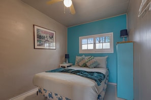 A bedroom with a bed, a window, a nightstand, a lamp, and a ceiling fan.