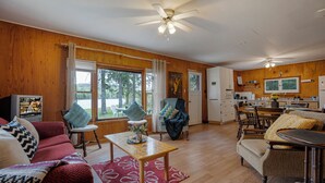 A spacious living area with a wooden floor, a dining table, and a kitchen in the background. - Sandy Shores Cabin on Lake St. Peter with Fire Pit+BBQ (Lake Saint Peter)