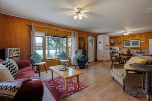 A spacious living area with a wooden floor, a dining table, and a kitchen in the background.
